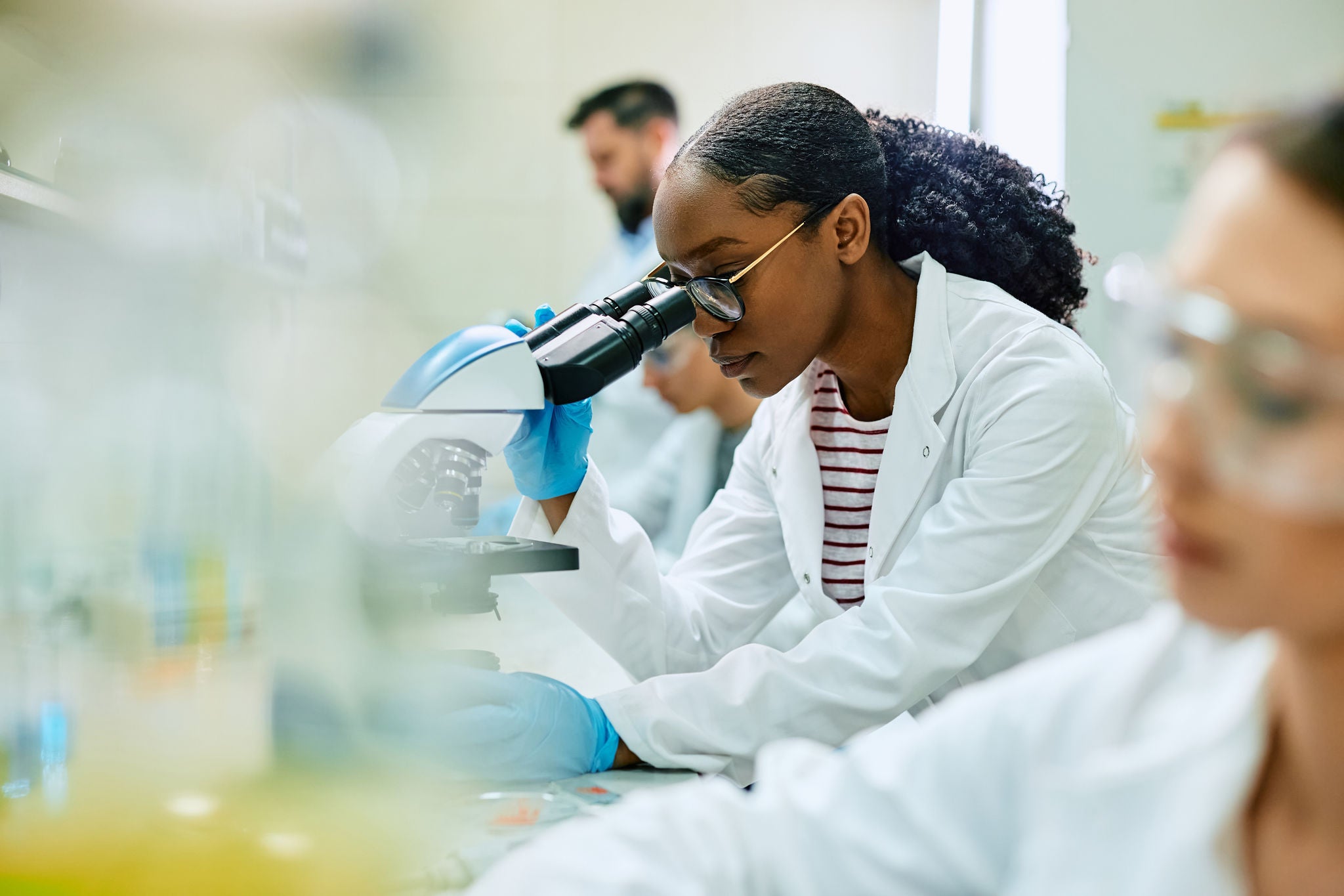 Black female scientist looking through microscope while working in laboratory.