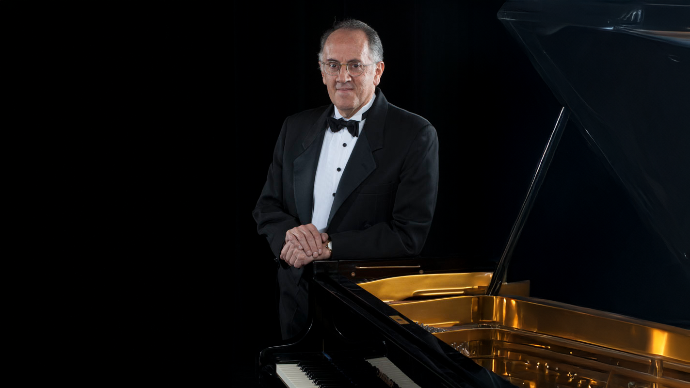 Claudio dressed up, standing next to his piano.