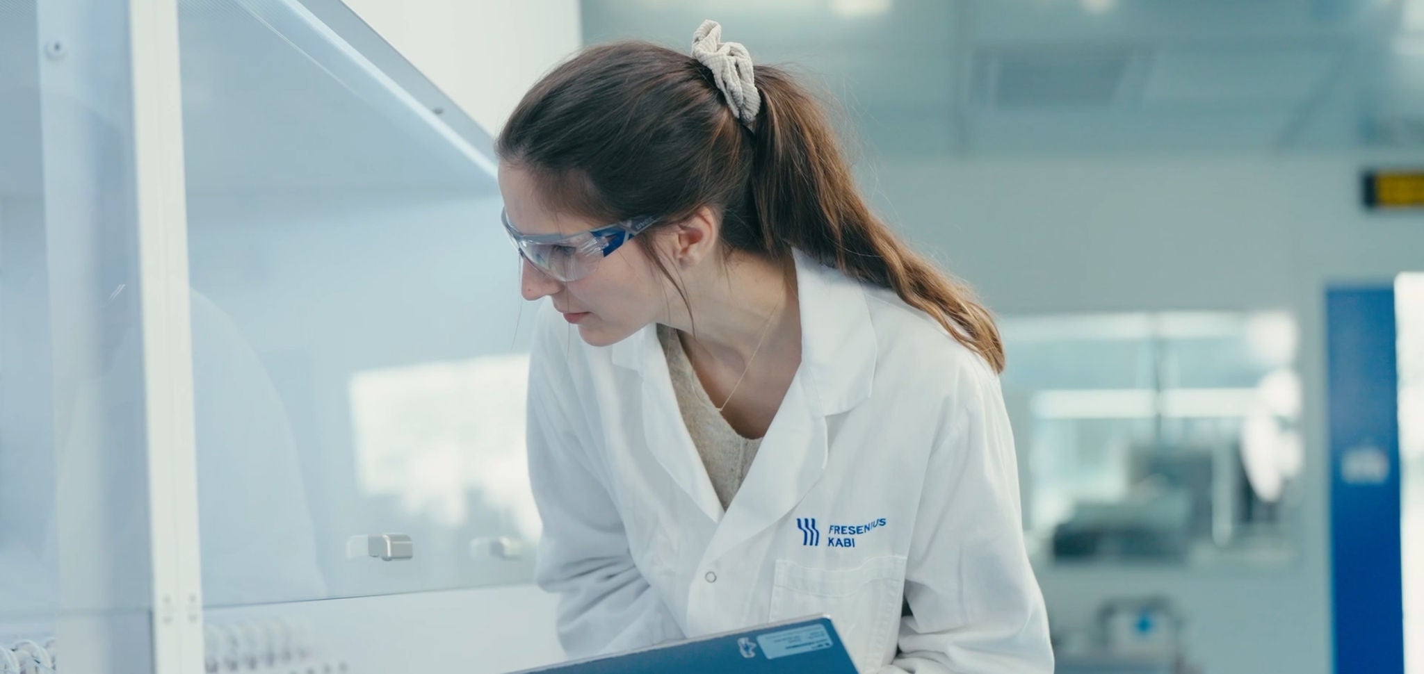 Laboratory professional wearing safety glasses and a lab coat examining equipment in a research laboratory.